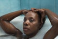 Portrait of African American woman, with her hands on her head and taking a bath with the bathtub full of foam, very relaxed. Royalty Free Stock Photo