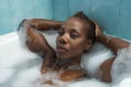 Portrait of African American woman, with her hands on her head and taking a bath with the bathtub full of foam, very relaxed. Royalty Free Stock Photo