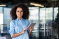 Portrait of an African-American woman standing in the office, holding a tablet in her hands, confidently and seriously Royalty Free Stock Photo