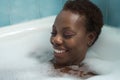 Portrait of African American woman, taking a bath with the bathtub full of foam, smiling happy and relaxed. Concept bath, relax, Royalty Free Stock Photo