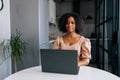 Portrait of African American young businesswoman sitting at table in modern kitchen room working on laptop, smiling Royalty Free Stock Photo