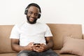 Portrait of an african american young guy enjoying listening to good music at home, sitting on the sofa, looking at Royalty Free Stock Photo