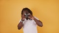 Portrait of an African man with braided hear and white shirt photographing with a vintage camera. on the orange