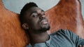 Portrait of African man sitting in chair, smiling and looking straight at camera. Male looks dreamy, thoughtful and calm