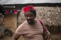 Portrait of An African Older Man in Red Muslim Taqiyyah Fez Hat posing with a stick for lame people on Yard Near the
