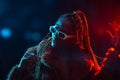 Portrait of an African young woman with braids wearing a coat posing under red and blue neon lights Royalty Free Stock Photo