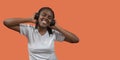 Portrait of african young woman listening to music on headphones with toothy smile, holding headphones with hands against orange Royalty Free Stock Photo