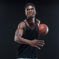 Portrait of afro american male basketball player playing with a ball over black background. Fit young man in sportswear Royalty Free Stock Photo