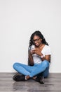 Portrait of afro american woman in casual sitting on floor with legs crossed and using mobile phone isolated over white background Royalty Free Stock Photo