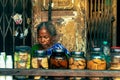 Portrait of an aged female tea seller under an old building with a variety of biscuits in front