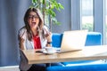 Portrait of aggressive brunette young woman in glasses sitting, looking at camera and showing middle finger fuck sign and