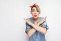 Portrait of alarming beautiful young woman in casual blue denim shirt with makeup and red headband standing with stop x sign and