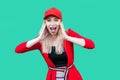 Portrait of amazed beautiful blond young hipster woman in red blouse and cap, standing, touching her face and looking at camera Royalty Free Stock Photo