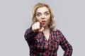 Portrait of amazed beautiful blonde young woman in casual red checkered shirt standing, pointing and looking at camera with Royalty Free Stock Photo