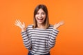 Portrait of amazed beautiful young woman with brown hair in long sleeve striped shirt. indoor studio shot isolated on orange Royalty Free Stock Photo