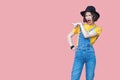 Portrait of amazed beautiful young woman in yellow t-shirt and blue denim overalls with makeup and black hat standing and pointing Royalty Free Stock Photo