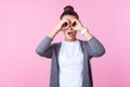 Portrait of amazed brunette teenage girl looking through fingers in binoculars gesture. studio shot on pink background