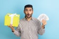 Portrait of amazed businessman showing dollar banknotes, cashback money and gift box.