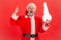 Portrait of amazed elderly man with gray beard wearing santa claus costume standing with open mouth, holding paper key, has idea Royalty Free Stock Photo