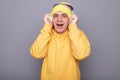 Portrait of amazed excited handsome man wearing beanie hat and yellow casual hoodie, listening to music with headphones, saying