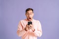 Portrait of amazed excited young man screaming after receiving good news on mobile mobile phone on pink isolated Royalty Free Stock Photo