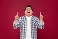 Portrait of amazed funny middle aged man in checkered shirt, eyeglasses standing, looking up, shocked face and pointing at up