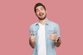 Portrait of amazed handsome bearded young man in blue casual style shirt standing, thumbs up and looking at camera with surprised