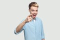 Portrait of amazed handsome young man in light blue shirt standing, accusing and looking at camera with surprised happiness face Royalty Free Stock Photo