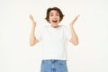 Portrait of amazed, happy young woman, raising hands up and looks surprised, standing excited against white background Royalty Free Stock Photo