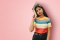 Portrait of an amazed indian asian girl student with big eyes posing  holding book on one side of her head and looking Royalty Free Stock Photo