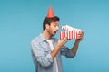 Portrait of amazed man with party cone hat opening gift, peeking inside box with surprised look, unpacking present