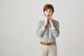 Portrait of amazed or shocked cute redhead woman with short haircut and freckles holding hands on chin, standing with