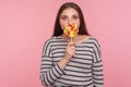 Portrait of amazed woman in striped sweatshirt licking lollipop, tasting sweet round rainbow candy with surprised expression