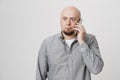 Portrait of amazed worried caucasian bald man talking on smartphone while looking aside with popped eyes and anxious