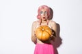 Portrait of amazed young party girl in pink wig, holding big pumpkin and looking left in awe, celebrating halloween Royalty Free Stock Photo