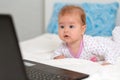 Portrait of amazement baby in sliders lies on the bed and looks at the laptop. The concept of teaching children to modern Royalty Free Stock Photo