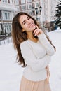 Portrait amazing joyful young woman with long brunette hair, white woolen sweater smiling on street full with snow