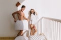 Portrait of amazing slim girl and funny boy cover himself with white pillow and laughing. Handsome man with tanned skin