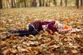 Portrait of teenage girl child wearing vinous sweater, yellow hat, checkered scarf, lying on yellow fallen maple leaves.