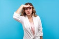 Portrait of ambitious businesswoman keeping curious look far away with hand over eye. blue background