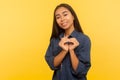 Portrait of amiable girl in denim shirt making heart shape gesture and smiling with kind friendly expression Royalty Free Stock Photo