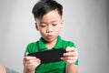 Portrait of an amused cute little kid playing games on smartphone isolated over gray background