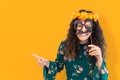 Portrait of amused girl with flower wreath on her head and fake mustache on yellow background Royalty Free Stock Photo