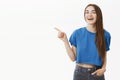 Portrait of amused happy good-looking female brunette in trendy blue cropped t-shirt pointing left and laughing joyfully