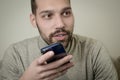 Portrait of an amused young man who is recording an audio message on his smartphone