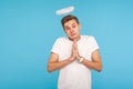 Portrait of angelic nice-looking man with halo above head holding hands in prayer and looking at camera