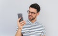 Portrait of angry bearded handsome businessman wears round spectacles and casual shirt, looks furiously into mobile phone, posing Royalty Free Stock Photo