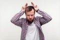 Portrait of angry bearded man showing bull horn gesture with puffed out cheeks to look more menacing. white background Royalty Free Stock Photo