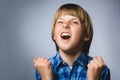 Portrait of angry boy in blue shirt with hands up yelling on gray studio background. Negative human emotion Royalty Free Stock Photo