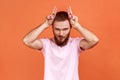 Man showing bull horn gesture with fingers over head, looking hostile and threatening. Royalty Free Stock Photo